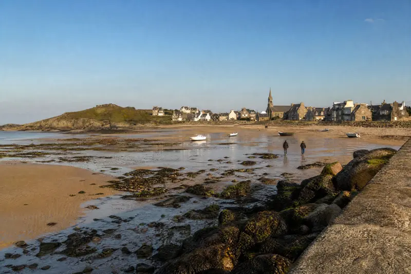 La Grande Plage à marée basse : un large estran de sable mouillé, des flaques, des rochers couverts d'algues et des bateaux posés sur le sable.
