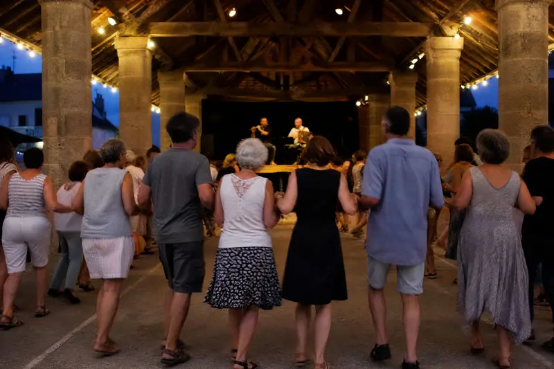 Un fest-noz sous la halle : une longue chaîne de danseurs, vus de dos, et des musiciens au fond.